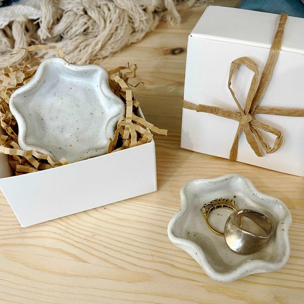 White ceramic ring dish with ruffle wave edge holding rings and earrings